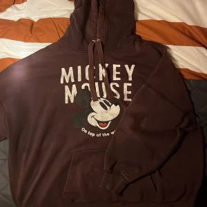 Brun Mickey Mouse hoodie - Säljer en supermysig brun hoodie med Mickey Mouse-tryck från Disney. Perfekt för alla som älskar klassiska karaktärer! Den har en ficka fram och en bekväm huva med dragsko. Passar perfekt för chilliga dagar eller som en statement piece i garderoben.