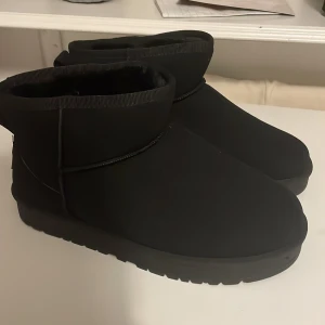 Svarta boots som liknar UGGS - Säljer ett par svarta boots i syntetmaterial med en cool etikett där det står 'Sport Best Fashion'. De har en robust sula med bra grepp och en enkel design utan snörning. Perfekta för höst och vinter när du vill hålla fötterna varma och stiliga. UGG kopior och säljs till mycket bättre pris. Storlek tror jag är 40-42