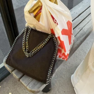 Svart axelväska med kedjedetaljer - säljer denna väska. På lilla brickan så står det Stella McCartney men vet ej om den är äkta. Perfekt för en dag på stan eller en kväll ute. Väskan har en stilren design och är lätt att matcha med olika outfits.