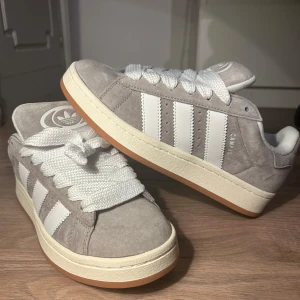 Adidas Campus - Säljer ett par snygga gråa Adidas Campus  i mocka med vita detaljer och breda snören. De har en klassisk design med de ikoniska tre ränderna på sidan. 🤩🤩Perfekta för vardagsbruk och ger en stilren look. Sulan är i en ljusare nyans som matchar perfekt med resten av skon. Original förpackning fraktas inte med. Hör av dig - Emil 🤙