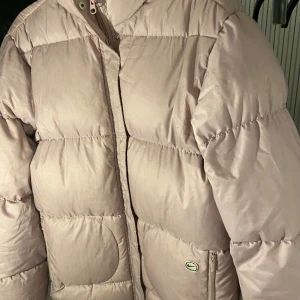 Beige/ljusrosa dunjacka från Nike - Säljer en vintage och varma dunjacka från Nike i storlek M. Perfekt för kalla dagar med sin pufferdesign och dragkedja. Jackan har en ljus insida och praktiska fickor. Den är i mycket bra skick och redo för vintern
