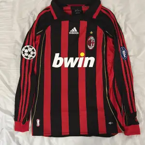 Säljer en AC Milan långärmad fotbollströja i svart och rött med Kaka's namn och nummer 22 på ryggen. Tröjan har Champions League-märken på ärmarna och är i nytt skick.