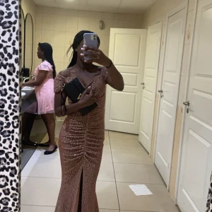 Glittrig axelbandslös klänning - Säljer en superfin glittrig klänning i en varm brun nyans. Den är axelbandslös och har en smickrande passform med en slits framtill. Perfekt för festliga tillfällen! Pris kan diskuteras vid snabb affär. Har bara använts en gång.