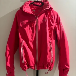 Rosa vindjacka från Helly Hansen - Säljer en snygg rosa vindjacka från Helly Hansen. Jackan har en dragkedja framtill och justerbar huva. Perfekt för blåsiga dagar och utomhusaktiviteter. Den är i mycket bra skick! Knappt använd.