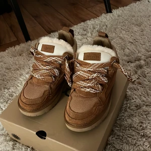 Ugg lowmel i färgen chestnut  - Säljer ett par snygga bruna sneakers från UGG i nytt skick. De har en mysig foder av päls och coola snören i vitt och brunt. Perfekta för höst och vinter med sin varma design. Skorna är i storlek dam 38 och kommer i originalkartong.
