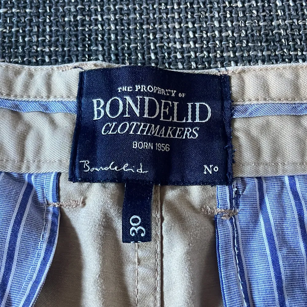 Säljer ett par stilrena beige byxor från Bondelid i storlek 30. De har en klassisk design med normal passform och är perfekta för både vardag och fest. Byxorna är i bra skick och har en snygg randig insida vid midjan. Perfekta för höst och vår! Pris går alltid att förhandlas!. Farkut & Housut.