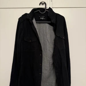 Svart skjorta från Filippa K - Säljer en stilren svart skjorta från Filippa K i storlek S. Skjortan har långa ärmar och knappar framtill samt två bröstfickor med knappar. Perfekt för både vardag och fest! 