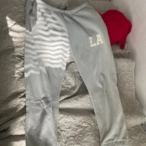 Gröna mjukisbyxor med LA-tryck - Säljer ett par gröna mjukisbyxor i storlek L med ett coolt 'LA'-tryck på ena benet. Byxorna har en elastisk midja med snörning för bästa passform. Perfekta för en avslappnad dag hemma eller en snabb tur till affären. Superbekväma och stilrena!