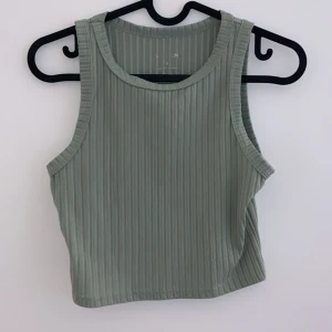 Grön ribbad linnetopp - Snygg grön ribbad linnetopp i ett mjukt och stretchigt material. Perfekt för sommardagar eller som ett lager under en jacka. Toppen är ärmlös och har en enkel, stilren design som passar till det mesta. Ett måste i garderoben för en avslappnad och trendig look!