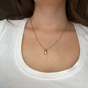 Elegant halsband med droppformad berlock - Säljer ett stilrent och elegant halsband med en vacker droppformad berlock. Perfekt för både vardag och festliga tillfällen. Kedjan är tunn och smidig, vilket ger en sofistikerad look. Passar perfekt som en fin detalj till din outfit.