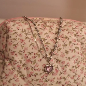 Halsband - Säljer ett vackert halsband med en hjärtformad rosa sten i mitten. Kedjan är silverfärgad och har små glittriga detaljer som ger en elegant touch. Perfekt för att piffa upp en outfit till fest eller speciella tillfällen. 💖