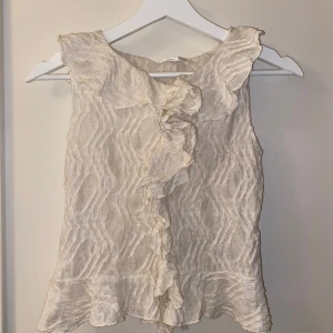 Beige ärmlös topp från Gina Tricot - Säljer en superfin beige ärmlös topp från Gina Tricot i storlek 158/164. Den har ett vågigt mönster och volangdetaljer framtill! Den är perfekt till sommaren och våren! Den är helt oanvänd och i strålande skick! Pris kan diskuteras.