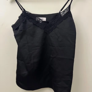 Svart linne från Kappahl - Snyggt svart linne från Kappahl i storlek S. Det har tunna axelband och fina spetsdetaljer.