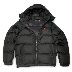 Svart dunjacka från Ralph Lauren - Säljer en snygg svart pufferjacka från Polo Ralph Lauren. Jackan har en dragkedja framtill och är långärmad med en broderad logga på bröstet. Perfekt för kalla dagar med sin varma och quiltade design. Passar både till vardags och lite finare tillfällen. Självfallet äkta, sista bild visar att den är äkta när man skannat QR koden, men även kvitto ifrån CareOfCarl finns! 