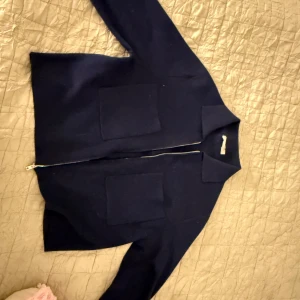 Mörkblå jacka/kofta med dragkedja - Säljer en stilren mörkblå jacka med dragkedja framtill. Jackan har en klassisk krage och två stora fickor på framsidan. Köpte på Åhléns för 600. 