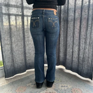 Blå bootcut jeans med nitar - Säljer ett par snygga blå bootcut jeans i bra skick. De är lågmidjade och har egensydda nitar på bakfickorna. Midjemått 38 cm grenmått 18.5 cm innerbenslängd 70 cm