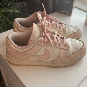 Nike Dunk i ljusrosa och vit - Säljer ett par Nike Dunk som är ganska slitna men fortfarande i fint skick att använda, använder de inte för att de är för stora för mig och inte min stil längre. Pris kan diskuteras 💕