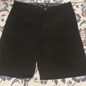 Säljer ett par svarta barn shorts i ny skick. De har en klassisk design med knapp och dragkedja framtill. Perfekta för sommaren och kan enkelt matchas med olika outfits. 