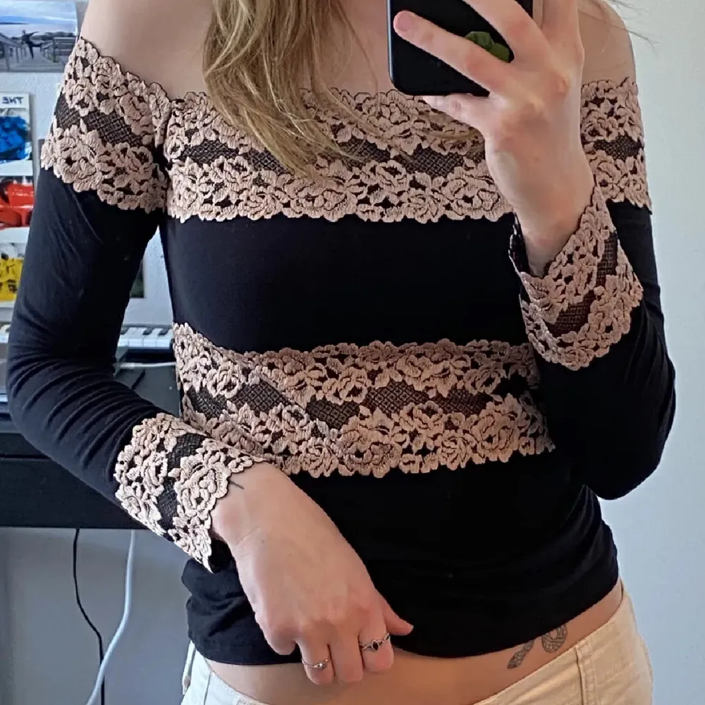 Säljer en snygg svart offshoulder topp med vackra beige spetsdetaljer. Toppen har långa ärmar och en tight passform, perfekt för både fest och vardag. Den är i mycket bra skick och ger en elegant touch till vilken outfit som helst. Är från intimissmi❤️. Toppar.