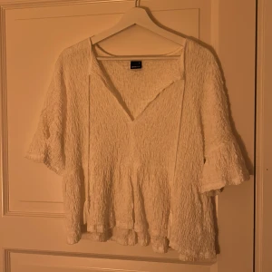 Vit blus från Gina Tricot - Säljer en vit blus från Gina Tricot i storlek XS. Blusen har en v-ringad design och är tillverkad i ett texturerat material som ger en unik look. Perfekt för en stilren och avslappnad outfit.