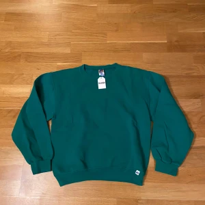 Grön sweatshirt från Russell - Säljer en klassisk grön sweatshirt från Russell. Tröjan har långa ärmar och en rund halsringning. Perfekt för en avslappnad stil. Den är tillverkad i ett mjukt material som känns skönt mot huden.