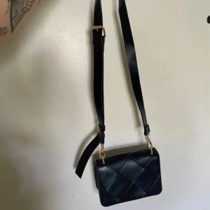 Svart quiltad axelväska - Snygg svart axelväska med quiltad design och justerbar axelrem. Väskan har guldfärgade detaljer och en stilren look som passar perfekt för olika tillfällen.