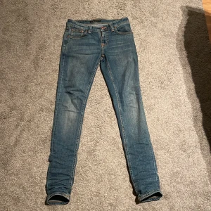 Blå jeans från Nudie Jeans - Snygga blå jeans från Nudie Jeans med en tight passform. De har klassisk femficksdesign och orange sömmar som ger en cool kontrast. Perfekta för en stilren look.