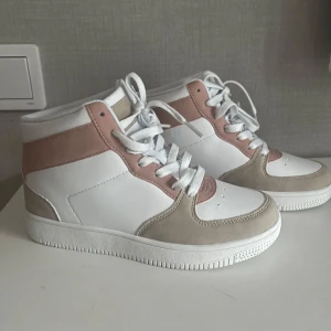 Vita och beige sneakers med rosa detaljer - Snygga sneakers i vitt med beige och rosa detaljer. Skorna har en hög modell med snörning och en bekväm sula. Perfekta för en stilren look.
