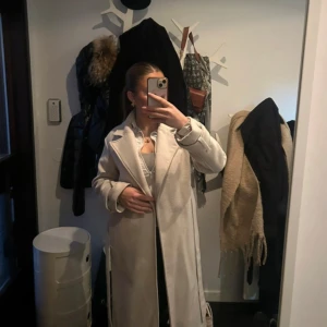 Vit  kappa - Snygg vit kappa med klassisk design och långa ärmar. Perfekt för att hålla stilen under kyligare dagar. Den har en stilren look som passar till många olika outfits.