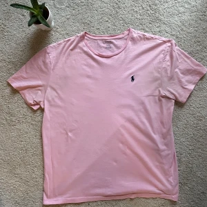 Rosa t-shirt från Ralph Lauren - Säljer en stilren rosa t-shirt från Ralph Lauren i väldigt bra skick. T-shirten är kortärmad och tillverkad i mjuk bomull. Perfekt för en avslappnad look.