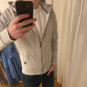 Grå zip hoodie - Säljer en stilren grå hoodie med dragkedja och huva från Jack&Jones. Tröjan har långa ärmar och en bekväm passform, perfekt för vardagsbruk. Den är tillverkad i ett mjukt material som ger en skön känsla.  Skriv om ni vill diskutera pris eller om ni har fler frågor!🙌