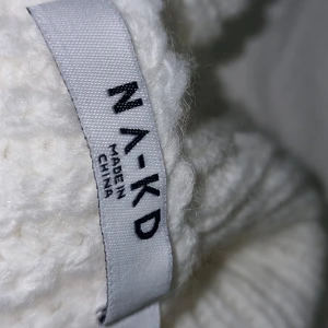 Vit stickad kofta från NA-KD - Säljer en mysig vit stickad kofta från NA-KD med knappar framtill. Perfekt för kyliga dagar och ger en stilren look. Koftan har långa ärmar och ribbade muddar.