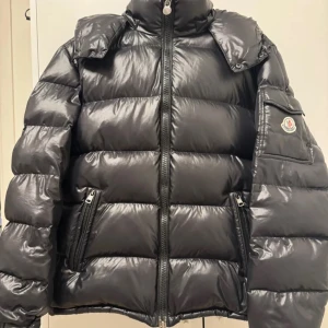 Svart pufferjacka från Moncler - Säljer en snygg svart pufferjacka från Moncler med glansig yta och dragkedja framtill. Jackan har långa ärmar och en hög krage för extra värme. Perfekt för kyliga dagar! 🖤nfc funkar