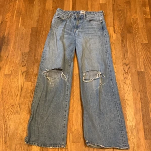 Blå jeans med slitna knän från 157 - Säljer ett par blå jeans från 157 med en cool, sliten look. De har vida ben och slitna knän för en avslappnad stil. Perfekta för en trendig vardagslook.