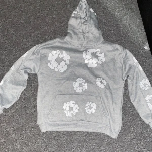 Denim Grå hoodie med blommönster - Säljer en grå denim hoodie tröjan är överallt på TikTok och det är svårt att köpa en i Sverige.Tröjan har en klassisk huva och en stor ficka framtill. Perfekt för en avslappnad stil. Helt ny