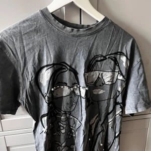 Grå t-shirt med tryck och pärlor - Snygg grå t-shirt med ett coolt tryck av två personer och dekorerad med pärlor. . Kortärmad och i mjukt material