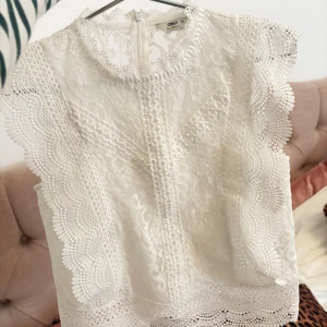 Vit spetsblus från Only - Säljer en elegant vit spetsblus från Only. Blusen har vackra spetsdetaljer och är ärmlös med en rund halsringning. Perfekt för en stilren look. Nypris 350kr använd 1 gång💕