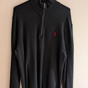 Svart tröja med dragkedja från Ralph Lauren - Snygg svart tröja från Ralph Lauren med halv dragkedja och röd broderad logga på bröstet. Varsamt använd fåtal gånger, säljes pga att jag har gått upp i vikt (pga gym). Det är medium i storlek och är true to size. Nypris 1600 från Zalando (kvitto finns)