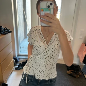 Vit prickig omlottblus - Säljer en jättefin prickig topp/blus i jätteskönt material! 🥰 toppen har ett knyte vid ena sidan så man kan göra att den sitter tajtare om det önskas🥰 Storlek S men skulle säga att den passar S och XS lika bra !🥰 skriv vid frågor  ( pris kan diskuteras) 