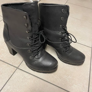 Svarta boots med snörning och klack - Snygga svarta boots i skinn med snörning och robust klack. Perfekta för en stilren look med en touch av edge. De har en stabil sula och är designade för att ge både stil och komfort.