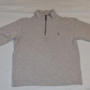 Grå tröja från Polo Ralph Lauren - Säljer en stilren grå tröja från Polo Ralph Lauren med dragkedja vid halsen. Tröjan har långa ärmar och en liten broderad logotyp på bröstet. Perfekt för en avslappnad och snygg look. Passar c 175cm 