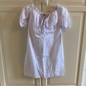 Klänning från NA-KD - Säljer denna snygga klänningen från NA-KD. Oanvänd. Storlek 40, men lite liten i storleken. Snygga detaljer vid axlarna och framtill. Off-shoulder. Färgen är vit. Finns en liten skavanker vid dragkedjan (se på sista bilden).