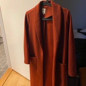 Roströd kappa - Vacker kappa i enkel modell, perfekt som ett fint mellanlager nu under hösten. Har fått lite noppor men som är enkla att ta bort med en noppmaskin. Kappan är i Petite-storlek vilket innebär att den är några cm kortare i ärm och längd.