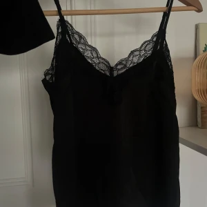 Svart linne med spetsdetaljer - Säljer ett elegant svart linne med vackra spetsdetaljer längs halsringningen. Perfekt för både vardag och festliga tillfällen. Linnet har en smickrande passform och tunna axelband som gör att justera. Obs storleken är xs med om man har större byst kan de sitta tight💞💞