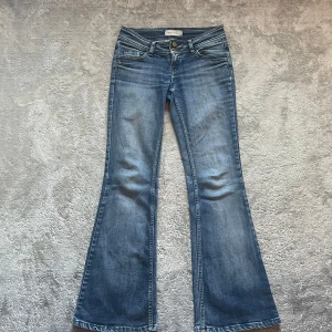 Blå bootcut jeans med broderade bakfickor - snygga blå bootcut jeans i bra skick med detaljer på bakfickorna. Jeansen är lågmidjade och har en bekväm passform som sitter snyggt över höfterna och låren innan de går ut i en bootcut. Midjemått 35cm🙂tveka inte på att skriva  vid frågor 