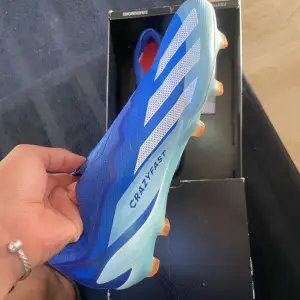 Säljer ett par snygga blå fotbollsskor från Adidas. De har en cool design med vita ränder och texten 'Crazyfast' på sidan. Skorna har en tight passform och är perfekta för snabba rörelser på planen. Kan gå ner vid snabbköp.