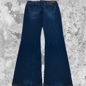 Mörkblå bootcut jeans från G-Star RAW - Säljer ett par snygga mörkblå bootcut jeans från G-Star RAW. De har en midwaist passform och är perfekta för både vardag och fest. Jeansen har två knappar i midjan och klassiska bakfickor. Superbekväma och stilrena!