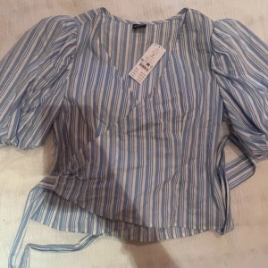 Fin blus  - Randig blus med vita och ljus blåa ränder, helt ny med prislapp!! Väldigt bra skick och jätte fin. Man knyter den samt så formar den kroppen väldig fint.