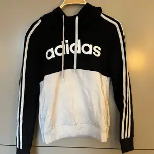 Säljer en snygg svart och vit hoodie från Adidas. Den har en klassisk design med Adidas-loggan tryckt på framsidan och de ikoniska tre ränderna längs ärmarna. Perfekt för en sportig look eller bara för att chilla. Den är i bra skick och superbekväm!