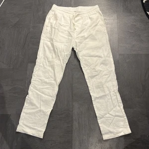 Vita linnebyxor i linne/bomullsblandning - Säljer ett par vita linnebyxor i en skön linne/bomullsblandning. De har en elastisk midja med snörning för extra komfort. Perfekta för varma sommardagar eller avslappnade tillfällen. Byxorna är i bra skick och redo för en ny ägare!